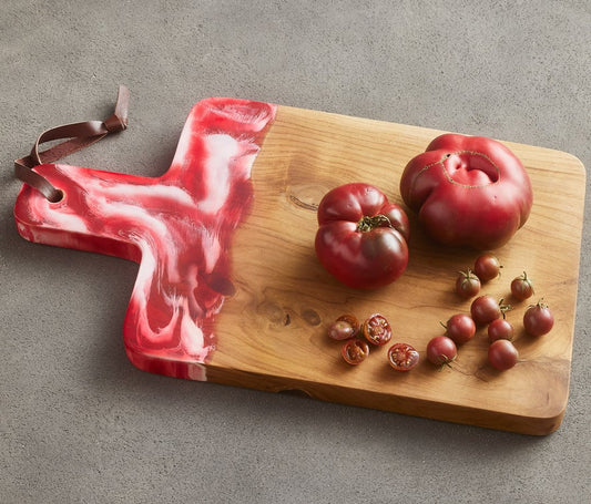 Teak board and resin handle are combined to create a one of a kind serving board. The handle is two-toned and hand-dipped in a berry color. Finished with a leather strap.